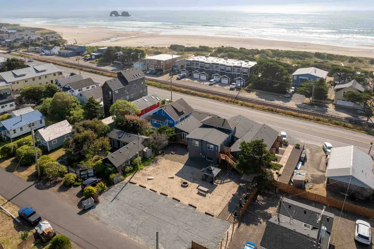 A wide view shows the ocean, sandy beach, and nearby colorful houses, with a visible play area and easy beach access paths. The vibrant setting reflects a lively, welcoming community with activity happening close to the shoreline.