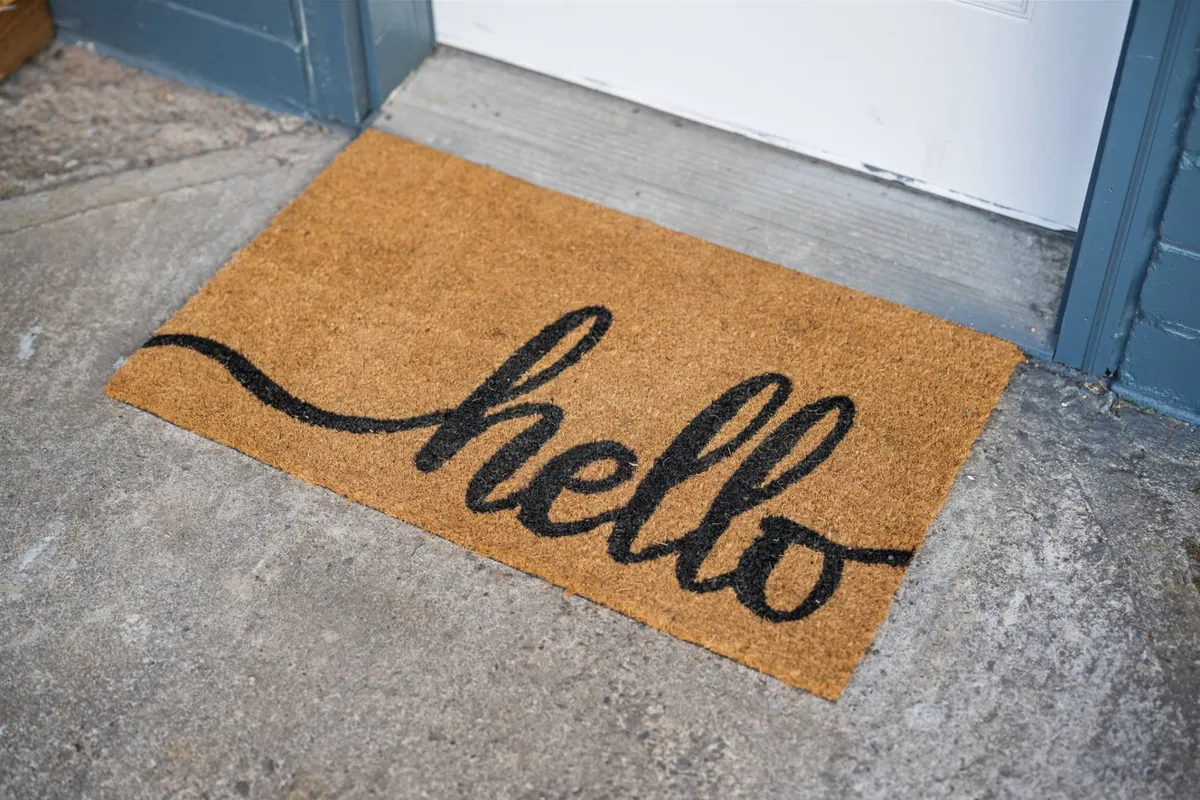 A charming exterior shot focusing on a welcoming doormat with the word 'hello,' set in front of an entryway. The image conveys warmth and the first impression as guests and their pets arrive.