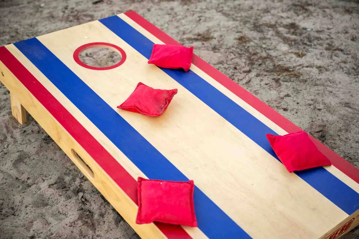An inviting exterior view features a vibrant cornhole board with red bean bags set up on a grassy area, suggesting opportunities for socializing and outdoor recreation. The communal setting hints at shared spaces where guests can mingle and unwind after a day of exploring the coast.
