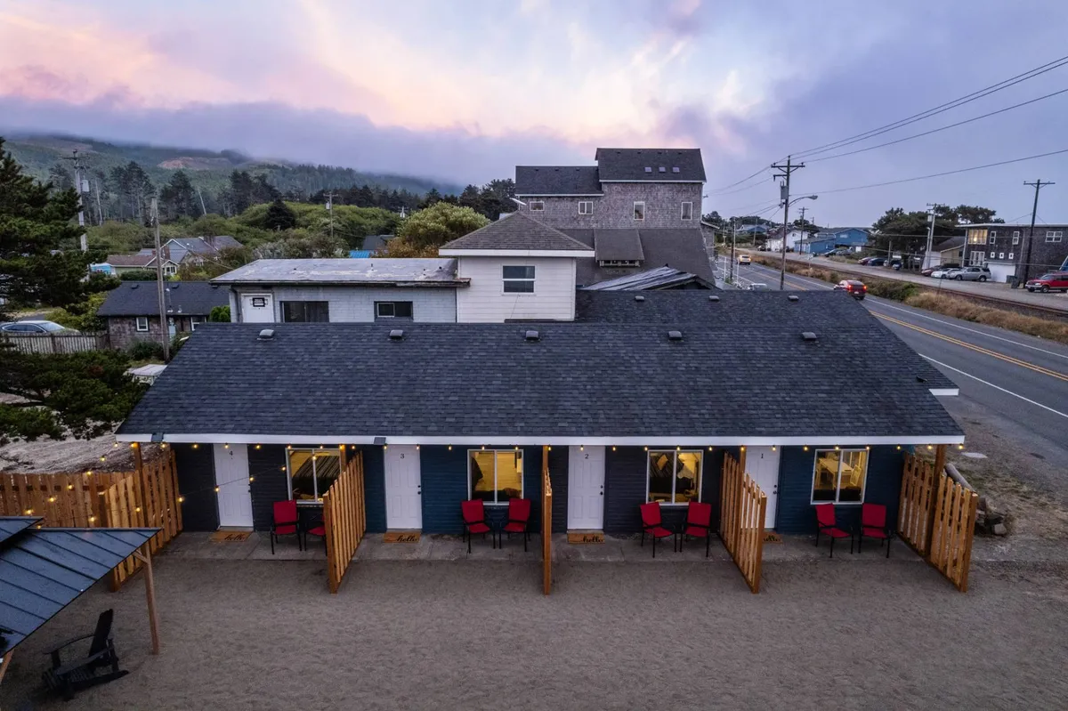 An exterior view of the building with red chairs set out on a sandy area in front. The scene exudes warmth and relaxation, ideal for unwinding outdoors and fostering spontaneous connections between guests.