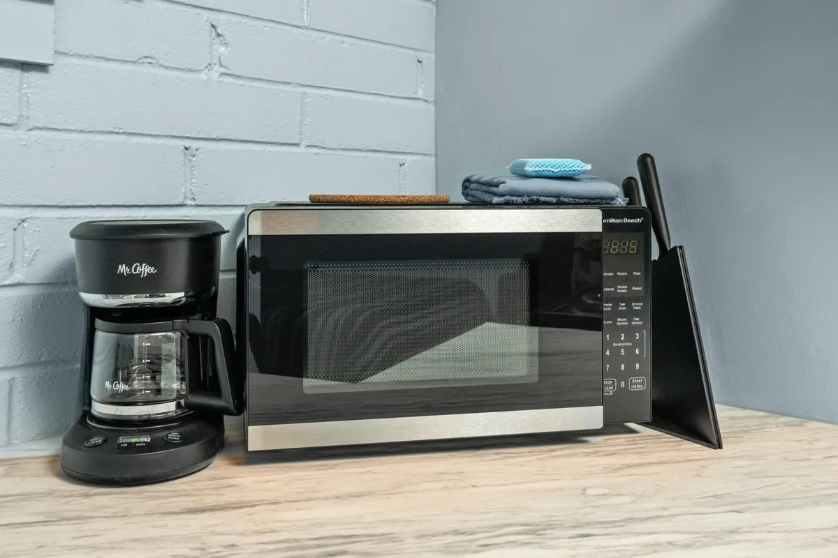 A cozy kitchen corner featuring a microwave, coffee maker, and dish towels. The scene feels approachable and practical, emphasizing small-scale meal prep and the ease of making coffee or reheating leftovers.