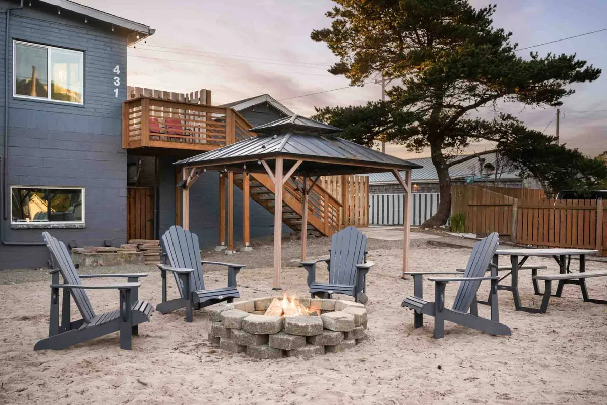 The photo showcases a shared gazebo surrounded by lush trees, with Adirondack chairs arranged around a fire pit. The gazebo and communal seating area invite group gatherings and socializing in a cozy, natural setting.