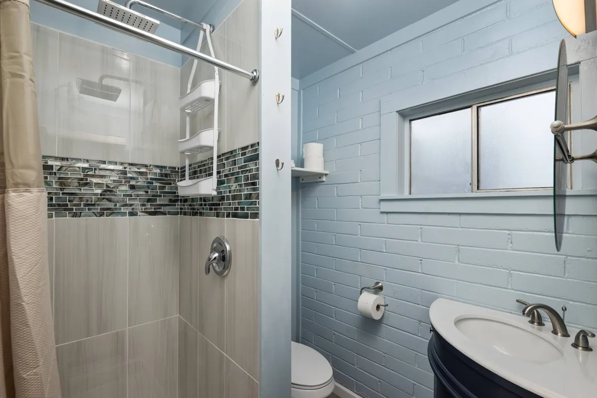 A modern bathroom with a spacious shower area, a vanity sink, and a window that allows sunlight to brighten the serene space. The clean design invites relaxation and self-care.