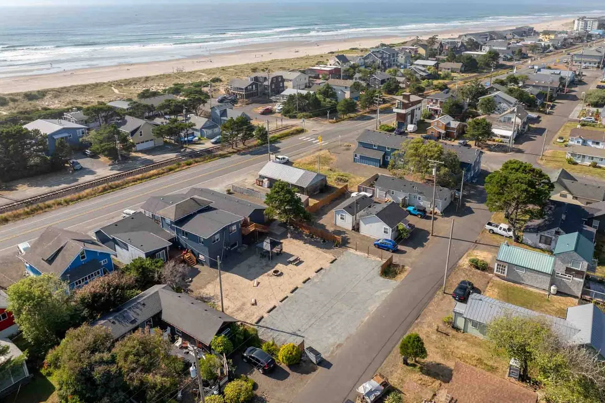 A relaxed scene captures the beachfront with houses, a road leading to the shore, and lush greenery. The atmosphere is calm and welcoming, suggesting morning walks, sunset beach strolls, and the inviting nature of the neighborhood.