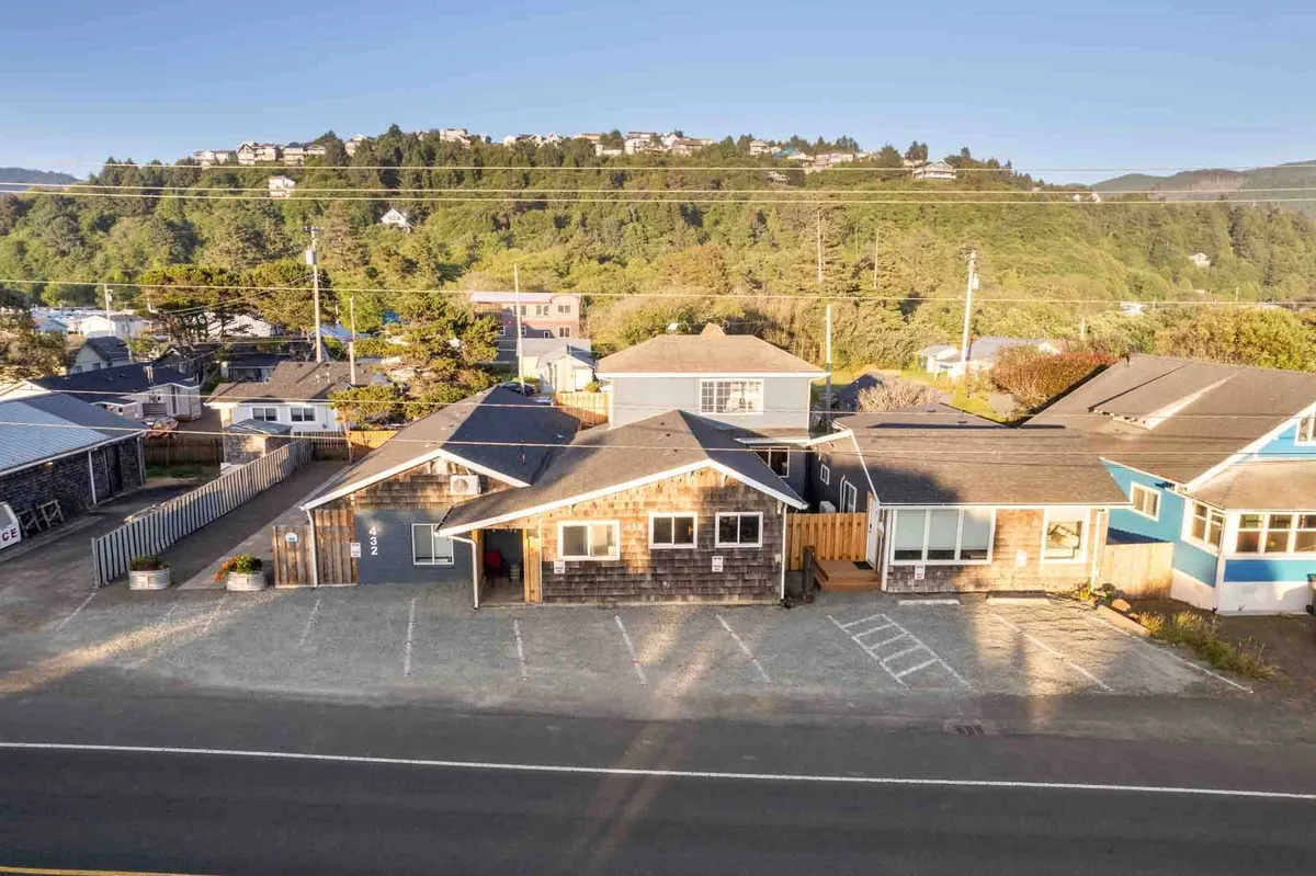 A wide exterior view of the main building with its classic shingle siding, ample parking area, and lush surrounding greenery. The welcoming garden space in the foreground invites guests to relax outdoors, while the golden light suggests sunset barbecues or stargazing evenings.